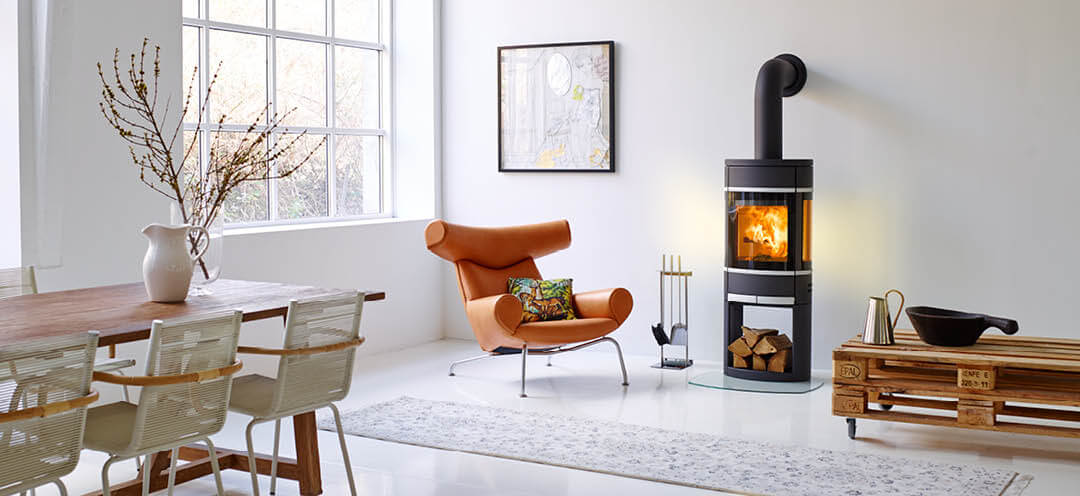 Czarny owalny piec na drewno Scan 68 w białym pokoju z designerskim krzesłem z jasnej skóry i szorstkim stołem z palet na kółkach