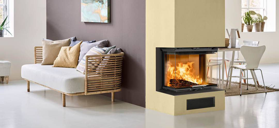 Kominek pomalowany na żółto w białym pokoju z kuchnią po jednej stronie i sofą po drugiej