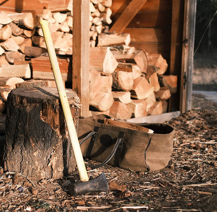 Siekiera opiera się o pieniek przy otwartej drewutni