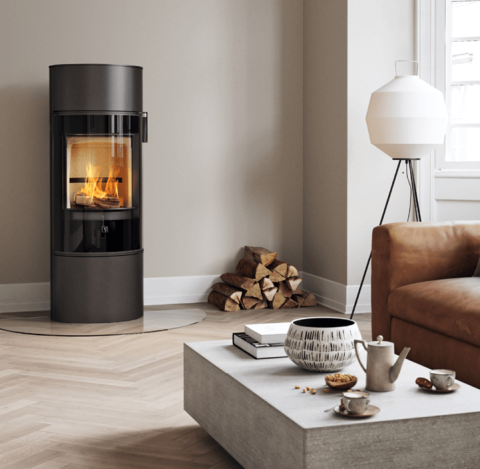 Czarny kominek Scan 84 z czarnymi szklanymi drzwiami W nowoczesnym skandynawskim salonie z brązową sofą i jasnoszarym krzesłem